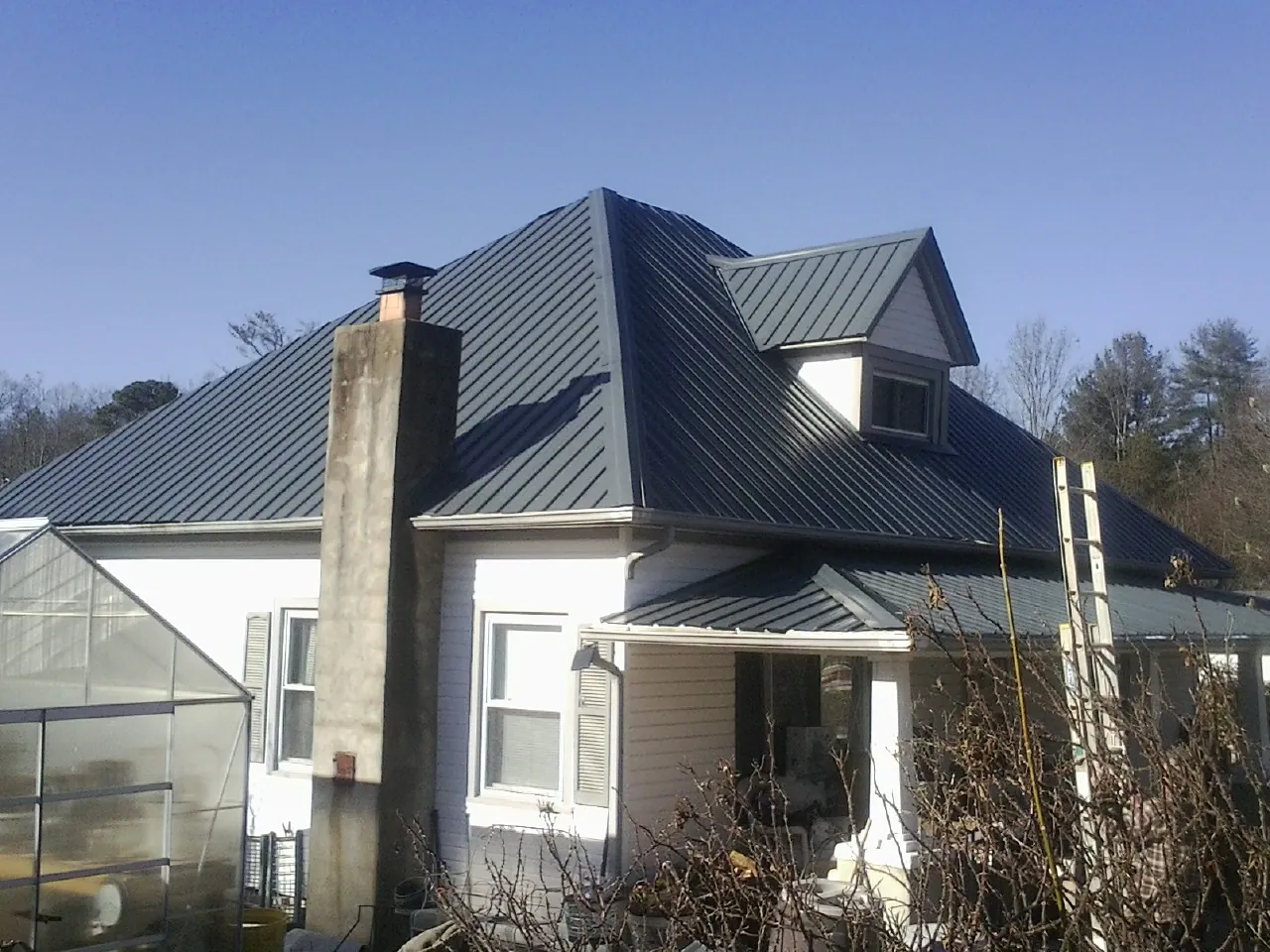 Dark blue standing seam metal roof on a white farmhouse with dormer — Slate & Tile Roof Repair by Roofing Brothers in Cummings