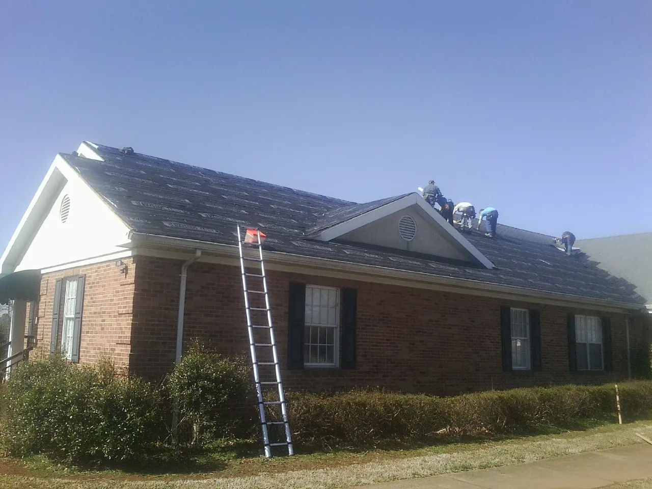 Crew tearing shingles off a brick ranch roof with a ladder set — Emergency Roof Repair work by our crew in Cummings