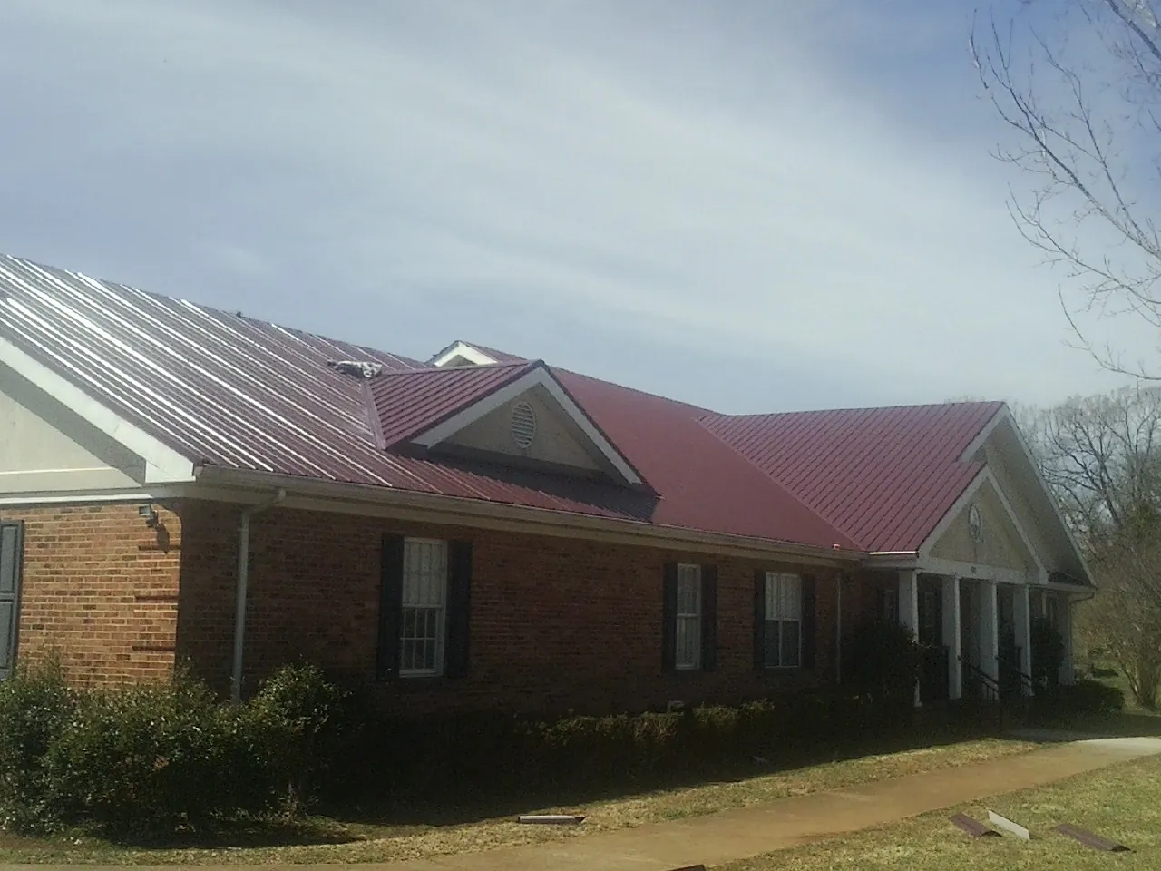 Red metal roof with gabled entries on a long brick building, from a Hail Damage Roof Repair job in Cummings