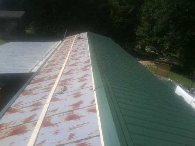 Old rusted panels beside newly installed green metal roofing — Wind Damage Roof Repair by Roofing Brothers in Cummings