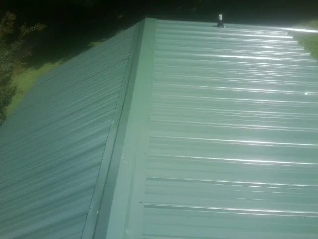 New green metal panels meeting at the ridge of a roof — Flat Roof Repair work by our crew in Cummings